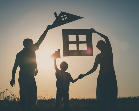This image shows a family of 3 holding a carton house.